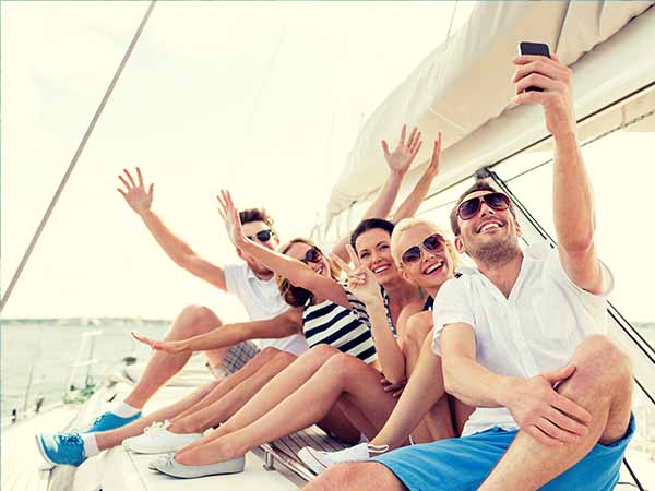 vacation, travel, sea, friendship and people concept - smiling friends sitting on yacht deck and making selfie