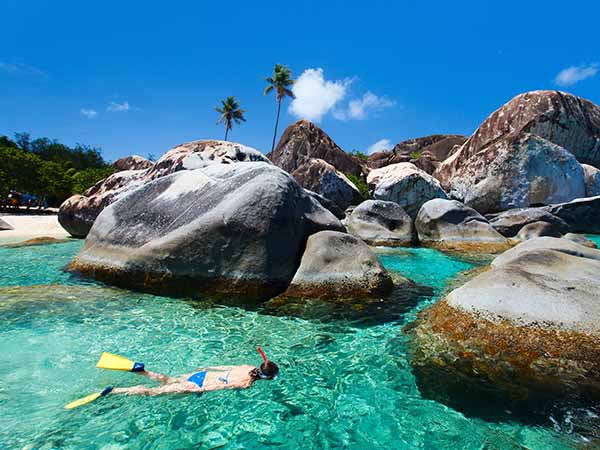 Young woman snorkeling in turquoise tropical water among huge granite boulders at The Baths beach area major tourist attraction on Virgin Gorda, British Virgin Islands, Caribbean
