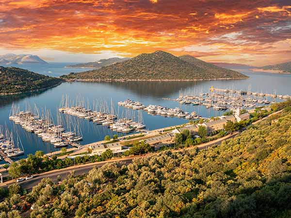 Yacht Marina. Top view aerial footage of many luxury boats and yachts in the harbor. Morning sunrise from behind the clouds. Mediterranean, Kaş, Antalya – TURKEY