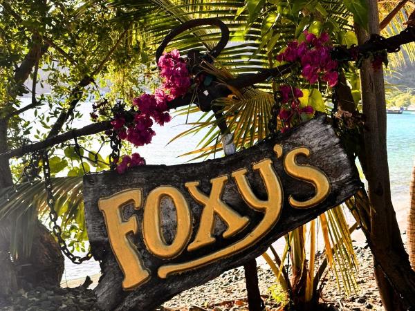 A wooden sign for Foxy's Jost van Dyke Bar surrounded by vibrant pink flowers.