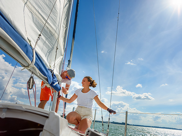Young man and woman sailing on a yacht. Female sailboat crewmember trimming main sail during sail on vacation in summer season