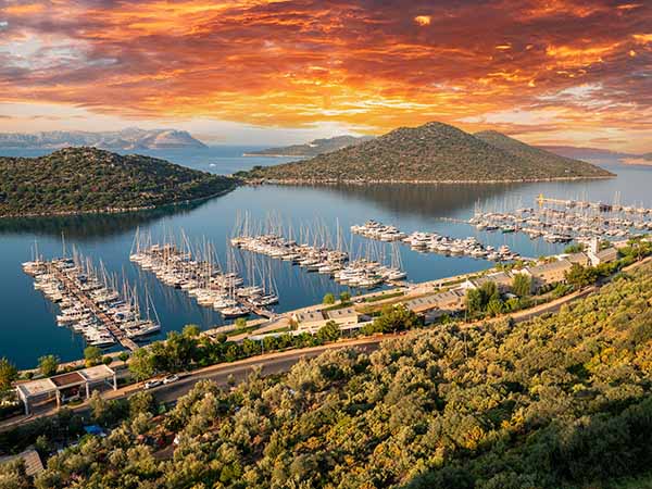 Yacht Marina. Top view aerial footage of many luxury boats and yachts in the harbor. Morning sunrise from behind the clouds. Mediterranean, Kaş, Antalya – TURKEY