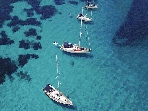 Aerial photograph of sailing yachts and a clear turquoise water in Cala Santa Maria, Sardinia.