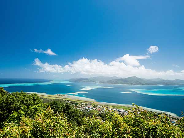 Scenic aerial view on lagoon with blue and turquoise water, green trees, barrier reef, blue sky and white clouds and airport of Raiatea island in French Polynesia